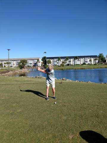 Woman golfing; holding golf club, aiming to put the ball, in golf course